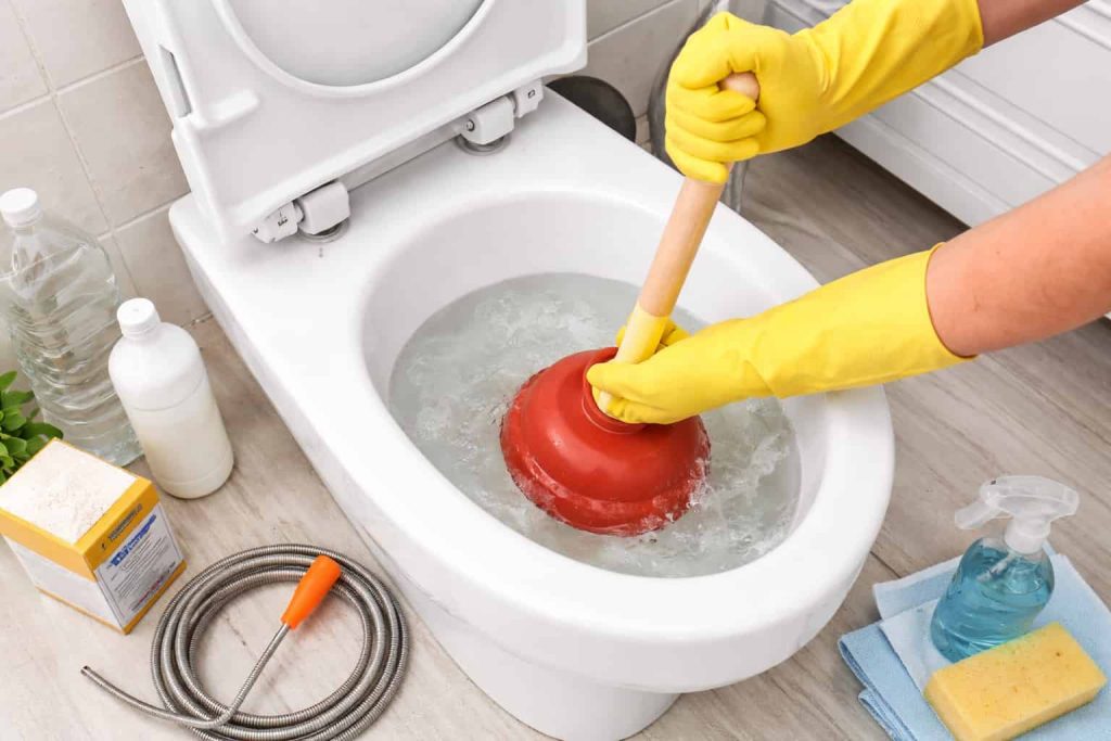 Un homme en train de déboucher des toilettes avec une ventouse rouge.